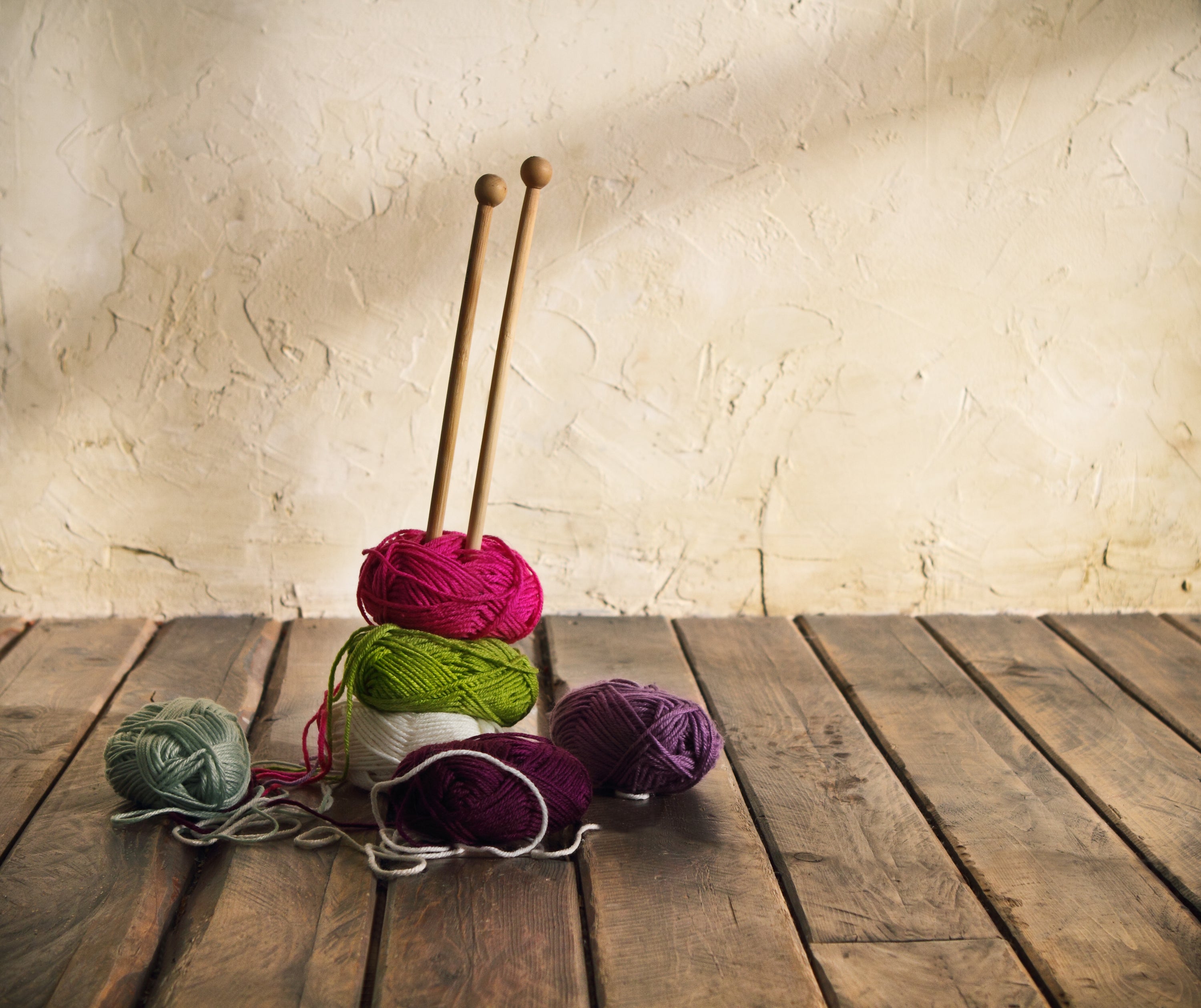 A small pile of different coloured yarns, with a pair of knitting needles sticking out of the top.