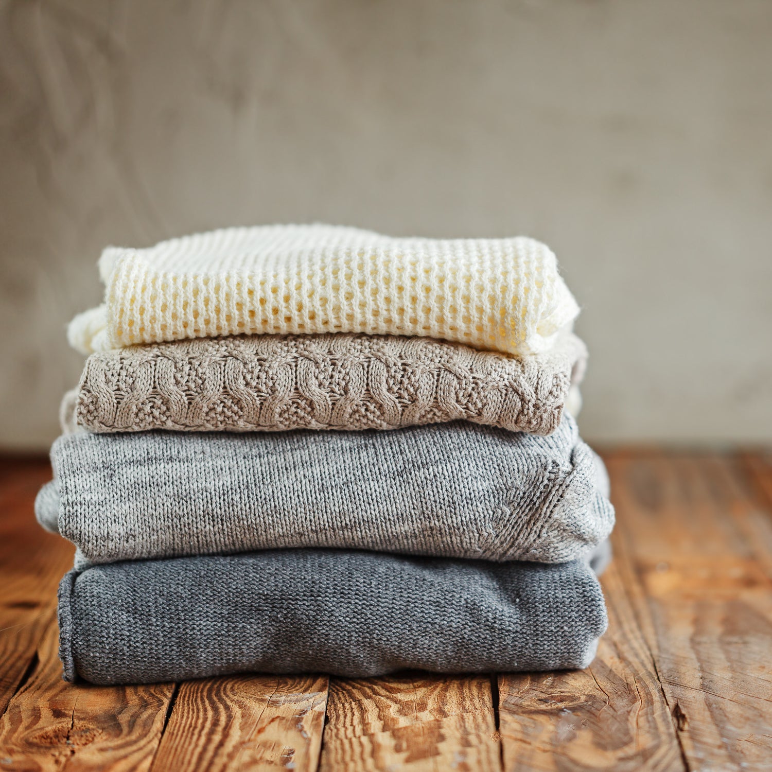 A neat pile of hand-knitted sweaters in neutral coloured wool.
