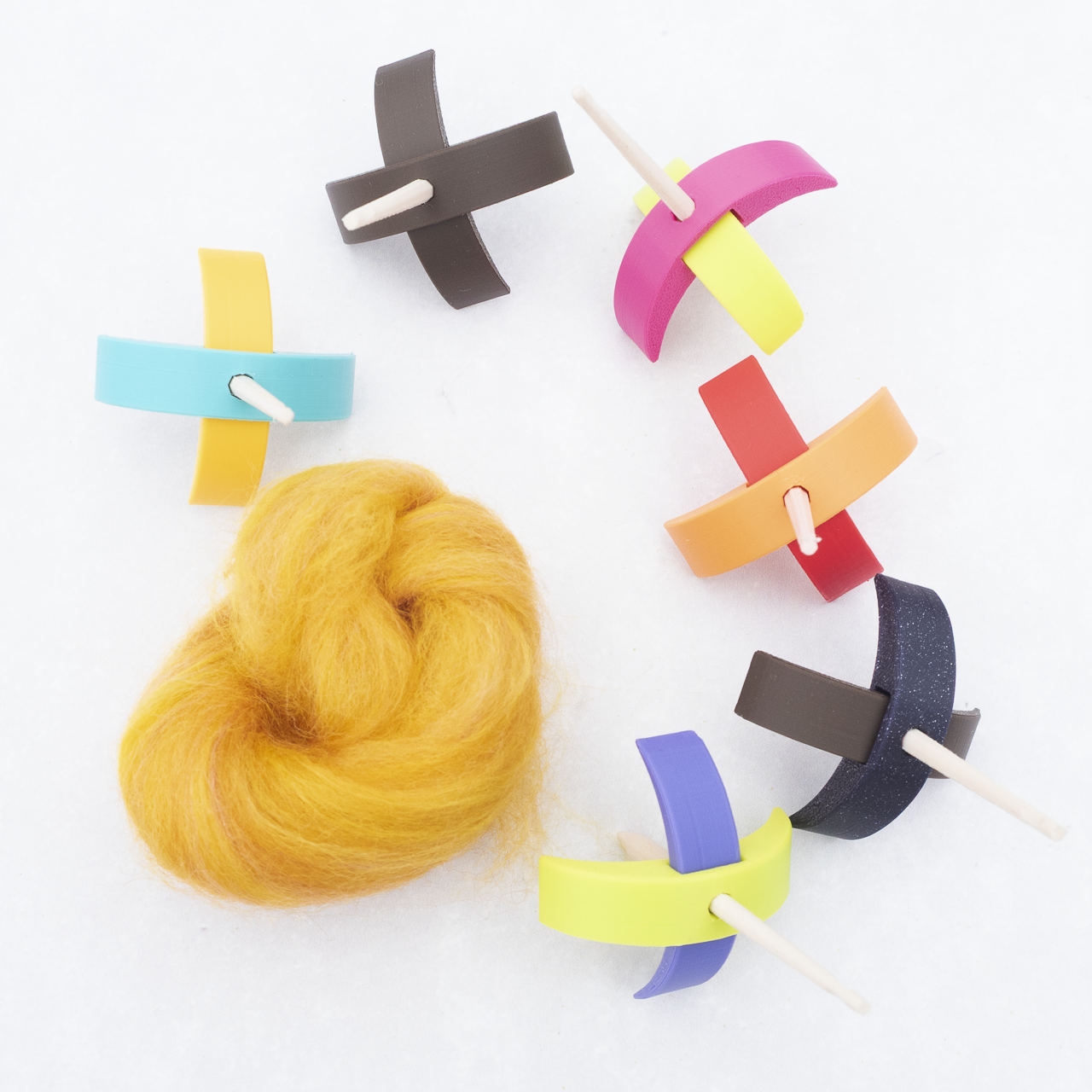 tiny 3d printed turkish spindles in various colours, shown next to a piece of unspun wool in a beautiful golden yellow