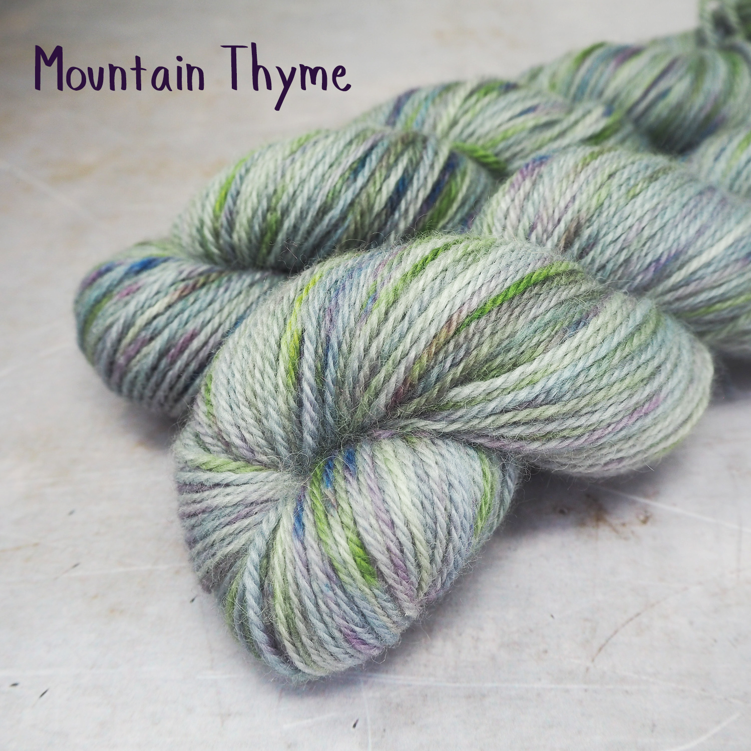 Two skeins of soft, DK-weight yarn, hand-dyed a a soft grey, and spekled with lime greed and violet.