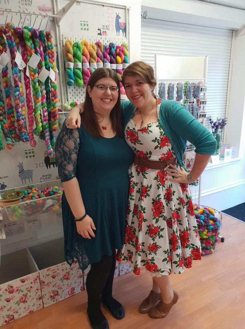 Katie stands next to a friend at her yarn shop. 