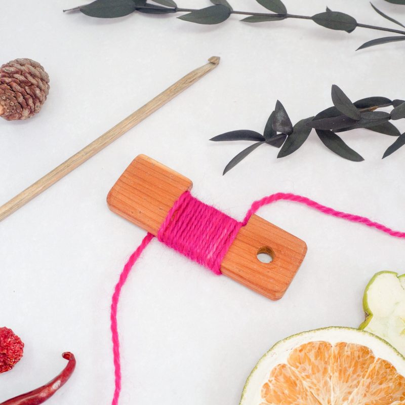 Pink yarn wrapped around an inch gauge, with a crochet hook. 