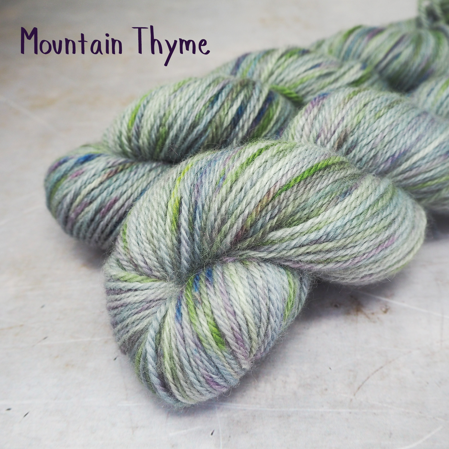 Two skeins of soft, DK-weight yarn, hand-dyed a a soft grey, and spekled with lime greed and violet. 